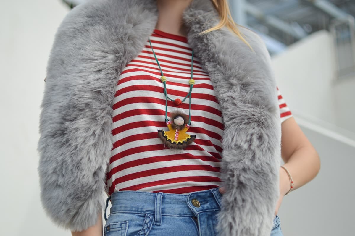 A red and white striped T-shirt styled with a grey faux-fur scarf, a pendant necklace and blue jeans